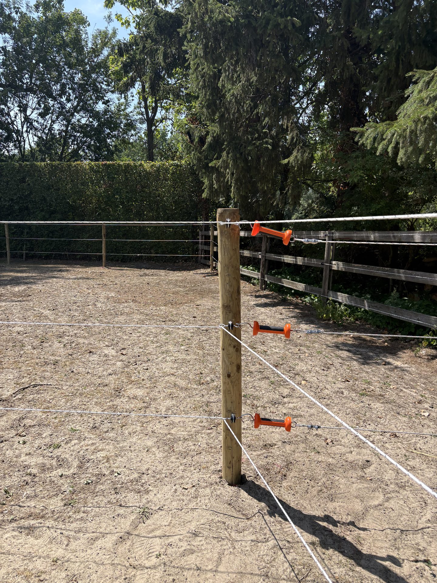 Orange electric-fence insulators and tensioners on a round wooden corner post